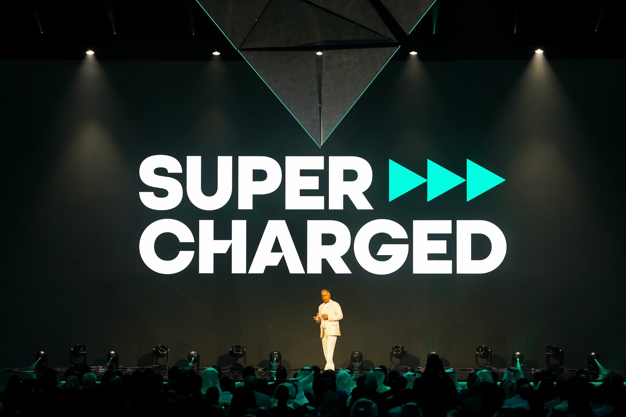 A speaker in white on stage beneath a giant illuminated Supercharged logo